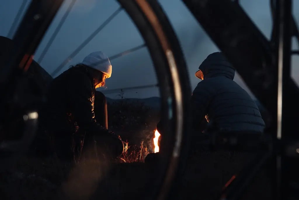 Cyclists sitting by a campfire at night during a bikepacking trip